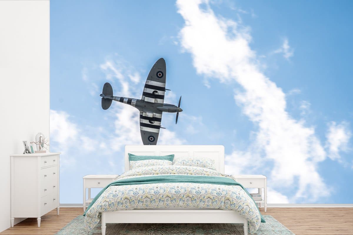 Behang - Fotobehang Een spitfire vliegtuig van onderen bij een wolkenlucht - Breedte 600 cm x hoogte 400 cm